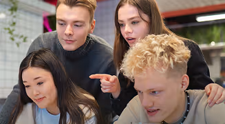 Four young adults gathered closely looking at a laptop screen, appearing engaged and focused.