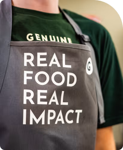Person wearing a gray apron with white text reading 'REAL FOOD REAL IMPACT' over a dark green shirt.