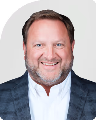 Smiling middle-aged man with beard wearing a white shirt and checkered blazer.