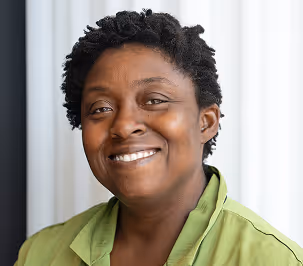 Smiling Black woman with short curly hair wearing a light green collared shirt against a neutral background.