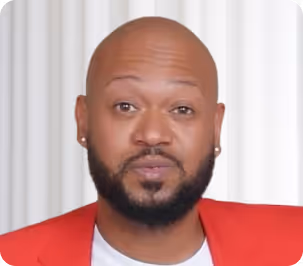 Portrait of a bald man with a beard wearing a red jacket and white shirt against a light background.