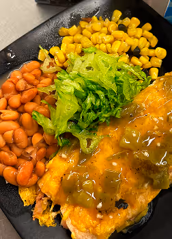 Plate with enchilada covered in green sauce, served with lettuce, pinto beans, and corn.