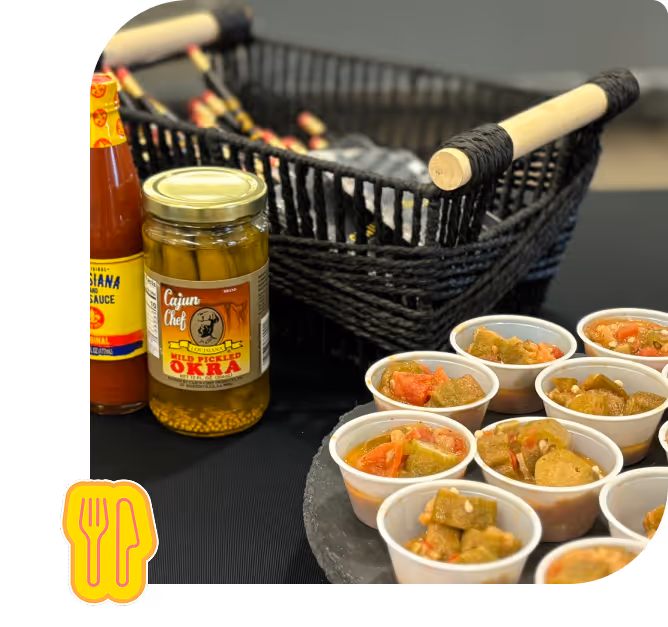 Multiple small cups filled with cooked okra and tomatoes, a jar of Cajun Chef mild pickled okra, and a bottle of Louisiana hot sauce on a table next to a black woven basket.