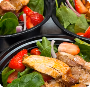 Bowls of salad with grilled chicken, spinach, strawberries, cherry tomatoes, and red onion slices.