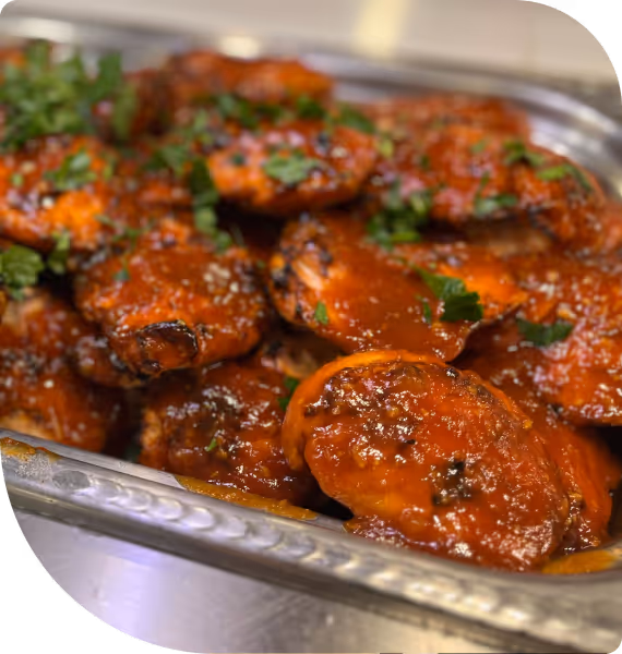 Tray of glazed chicken wings garnished with chopped parsley.