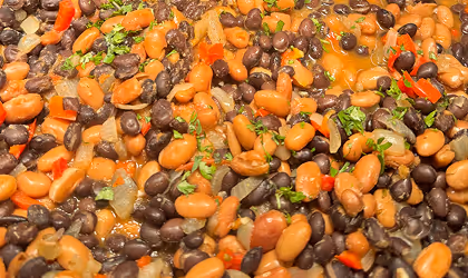 Close-up of cooked mixed beans with chopped herbs and red pepper pieces.