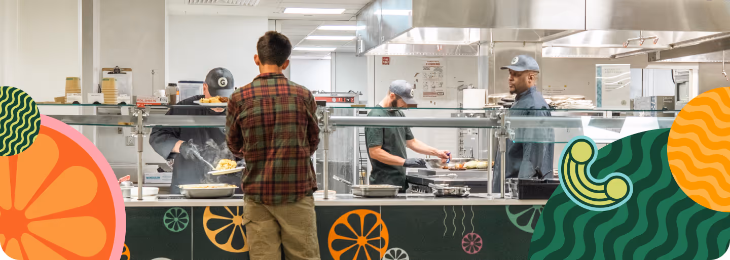 Man in plaid shirt ordering food at a counter where three workers prepare meals in a commercial kitchen.