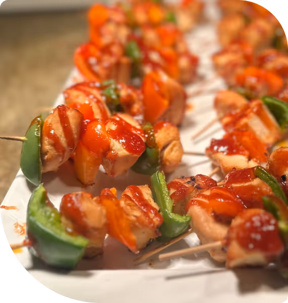 Close-up of skewers with grilled chicken, green bell peppers, and red sauce on a white plate.