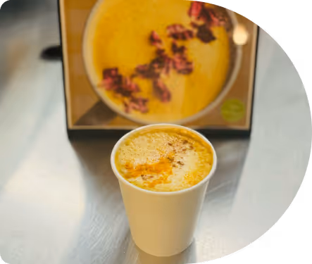 Paper cup filled with a frothy turmeric latte sprinkled with spices on a reflective surface.