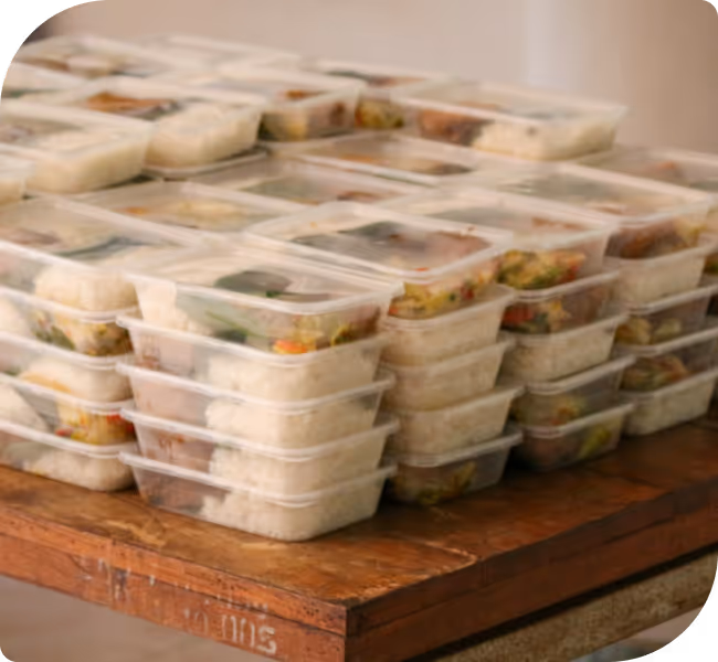 Stacks of clear plastic meal prep containers filled with rice and mixed vegetables on a wooden table.