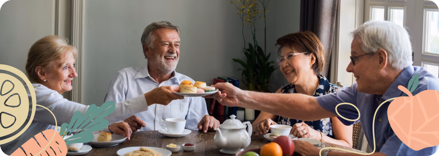 Four older adults sitting around a table sharing scones, tea, fruit, and cookies in a cozy room.