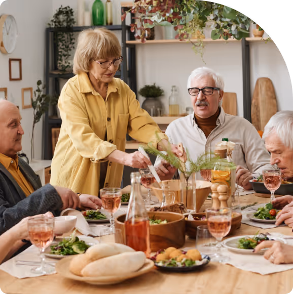 Group of elderly people enjoying a meal together around a wooden table with salads, bread, and rosé wine.