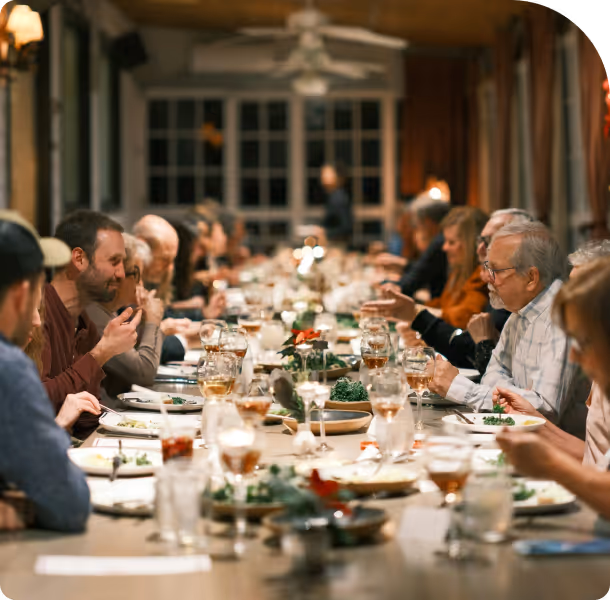 Large group of people seated at a long dining table enjoying a meal together in a warmly lit room.