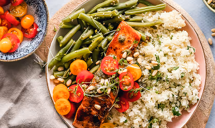 Plate with grilled salmon, steamed green beans, cauliflower rice, cherry tomatoes, and pine nuts.