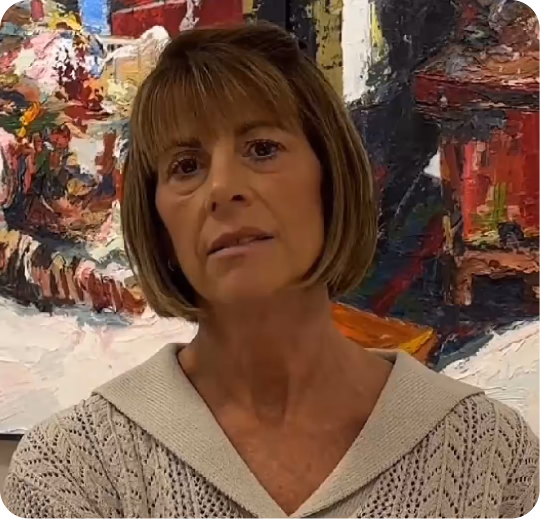 Woman with short brown hair wearing a beige knit sweater, standing in front of a colorful abstract painting.