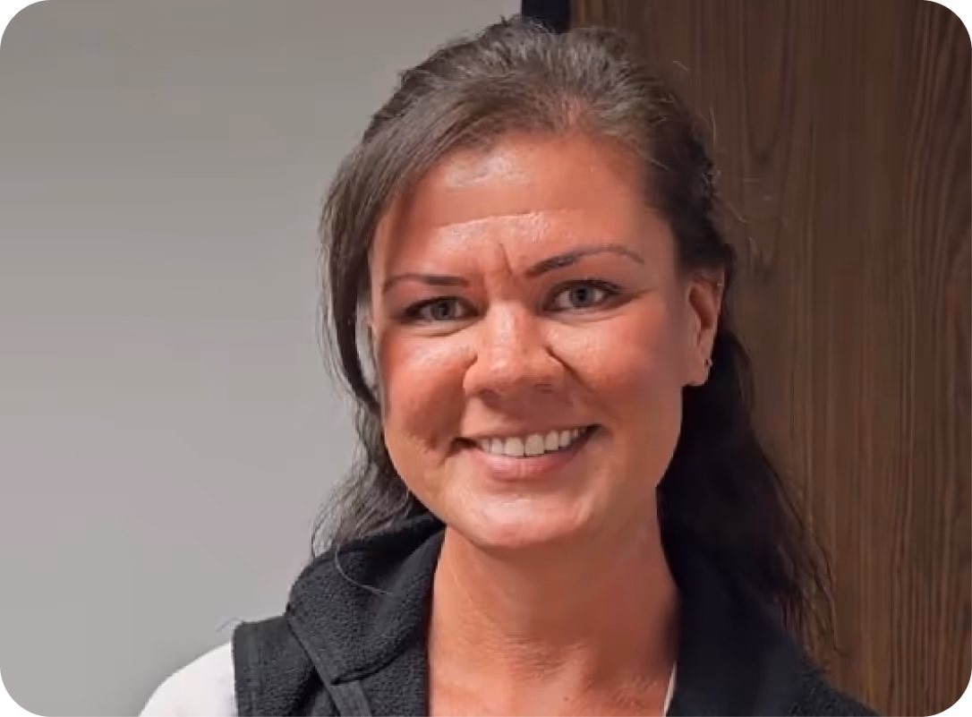 Smiling woman with dark hair wearing a black vest and white shirt against a neutral background.