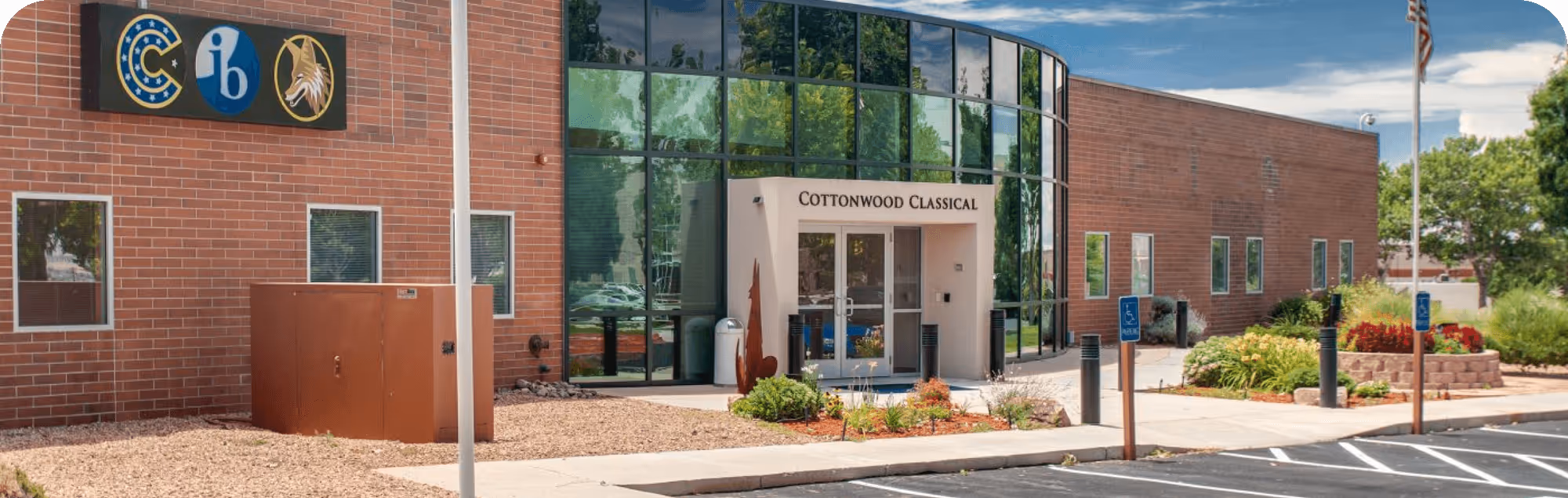 Entrance of Cottonwood Classical school with brick walls, curved glass windows, and landscaped garden areas.