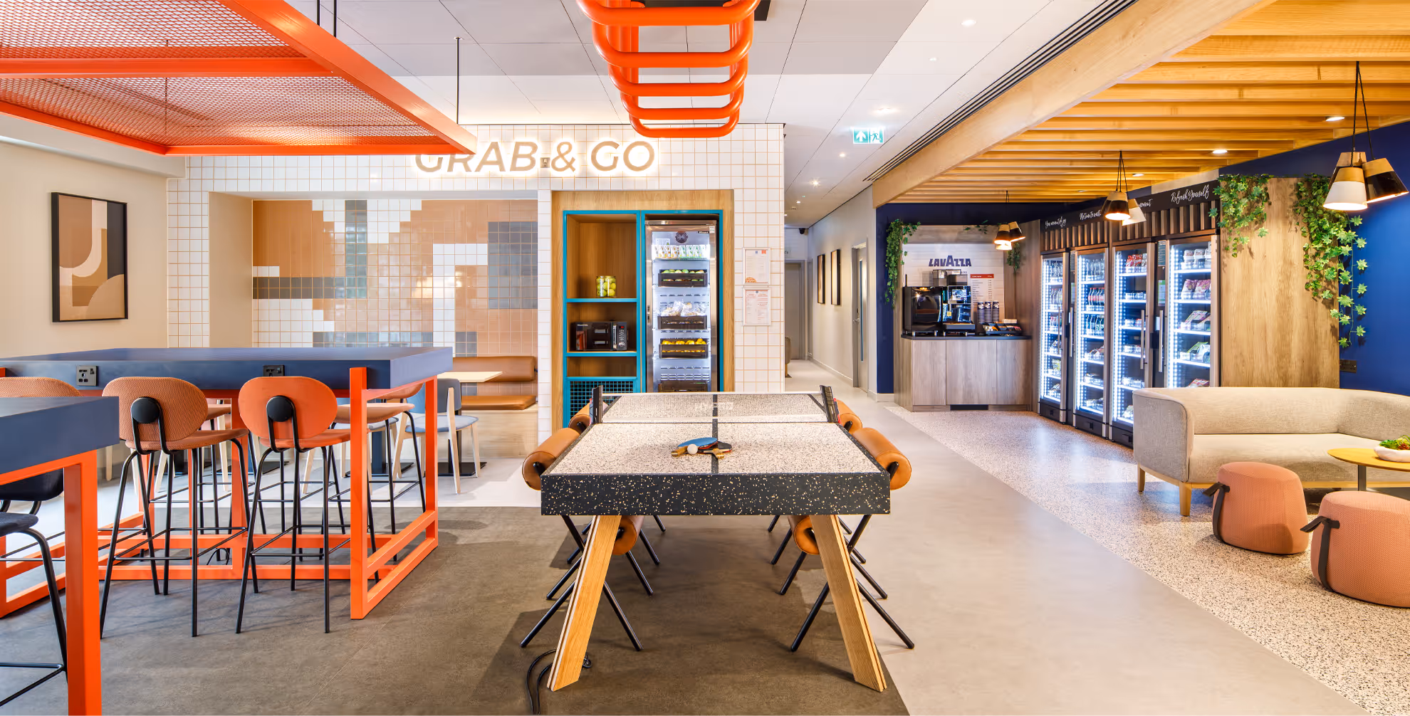 Common area at Ibis Budget Manchester Airport, showing shome chairs, sofas and desks.