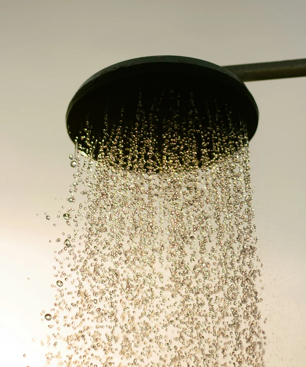 Close-up of a black shower head spraying water against a neutral background