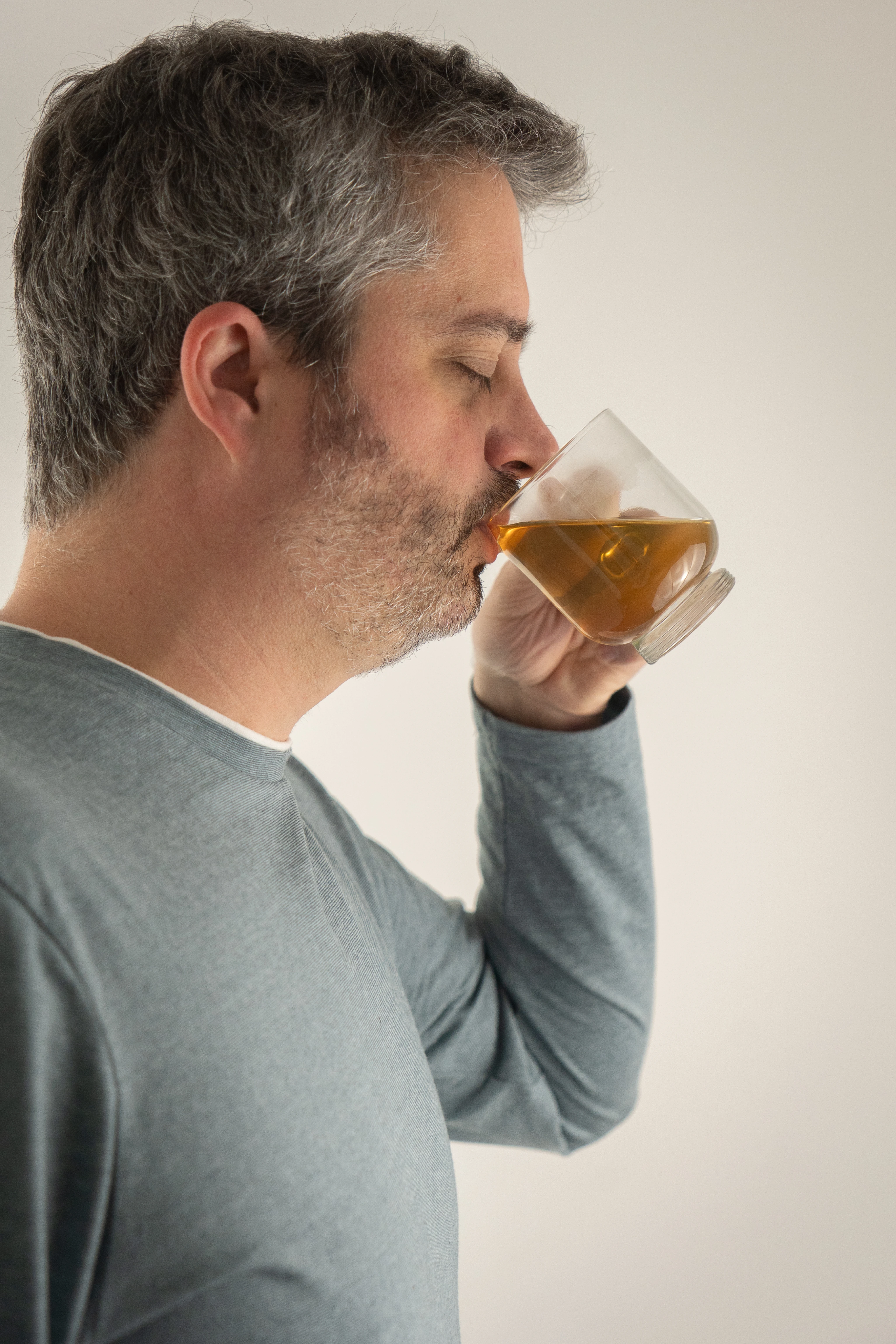 Homme aux cheveux gris et barbe courte buvant une tasse de thé.