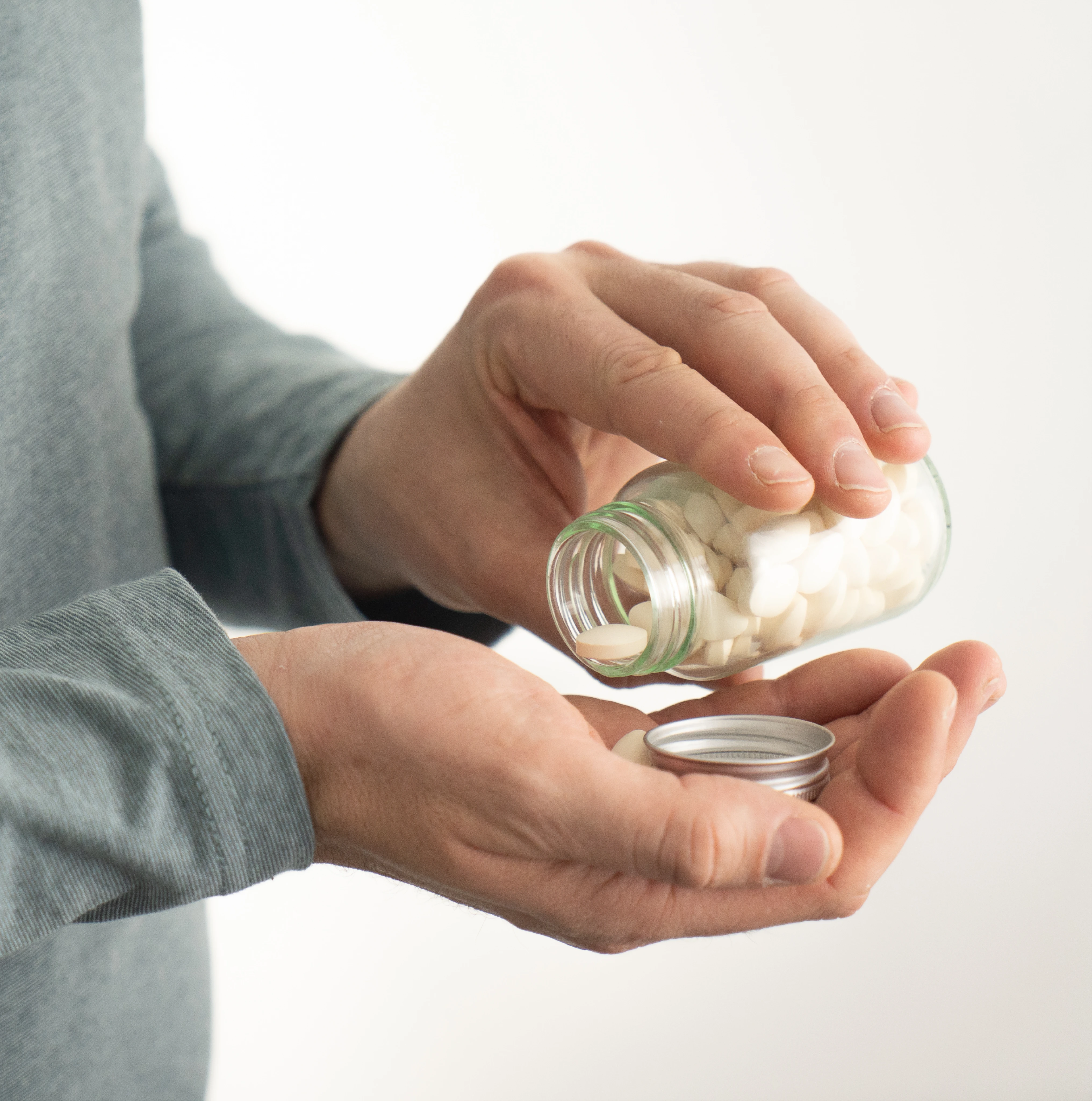 Une personne versant des comprimés blancs d'un petit flacon en verre dans sa main.