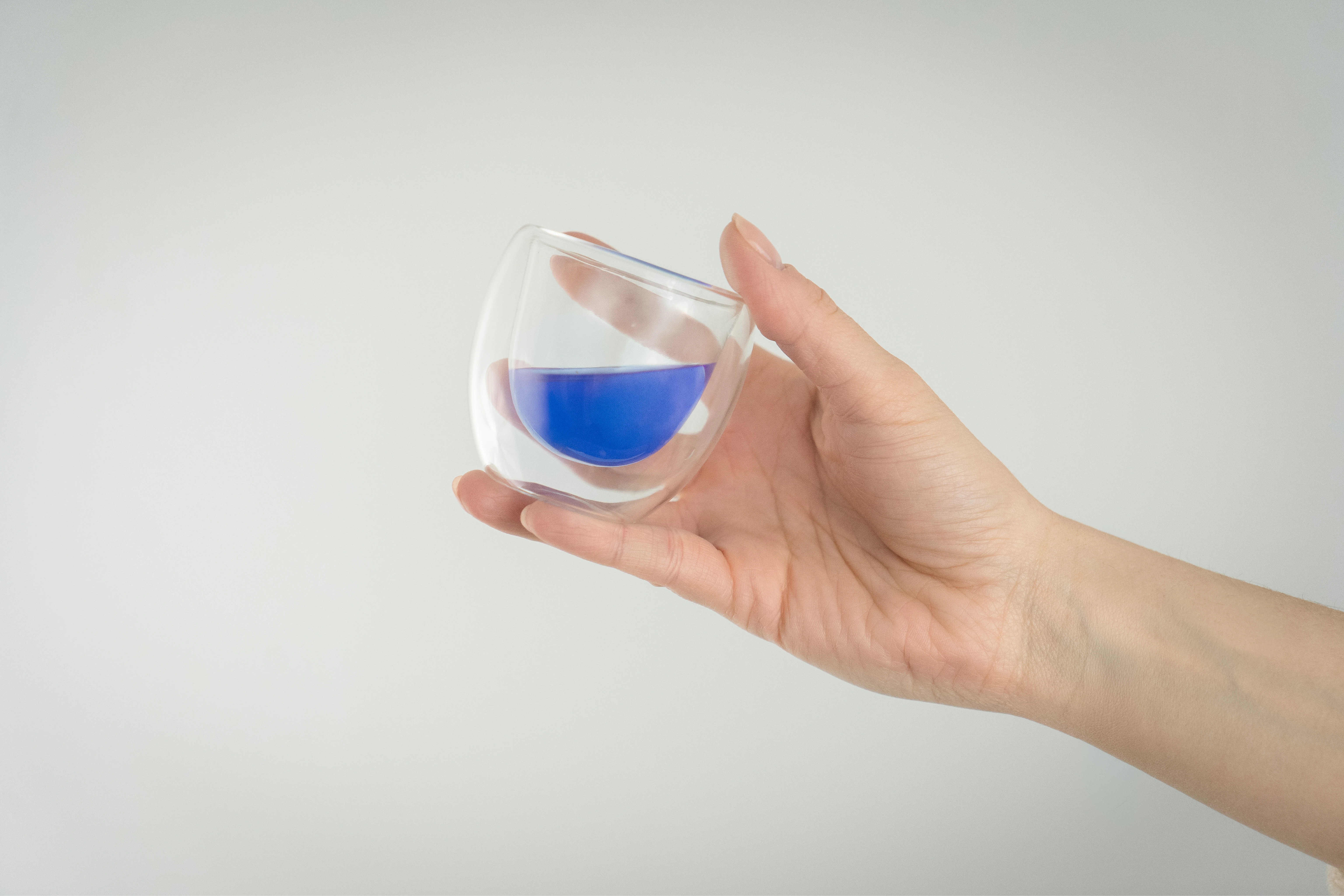 Main tenant un petit verre en double paroi contenant un liquide bleu.