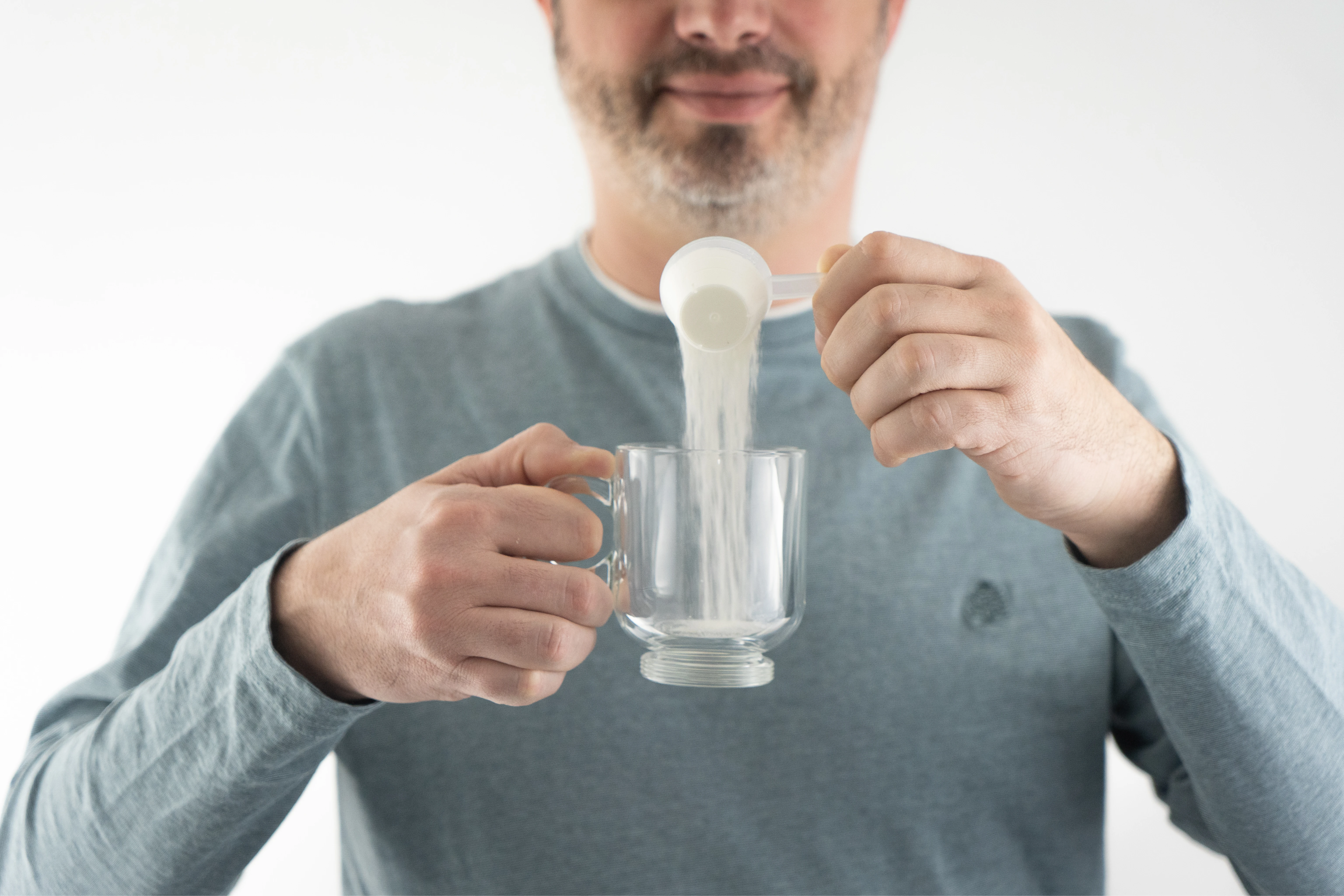 Homme versant une poudre blanche d'une cuillère dans une tasse en verre transparente.