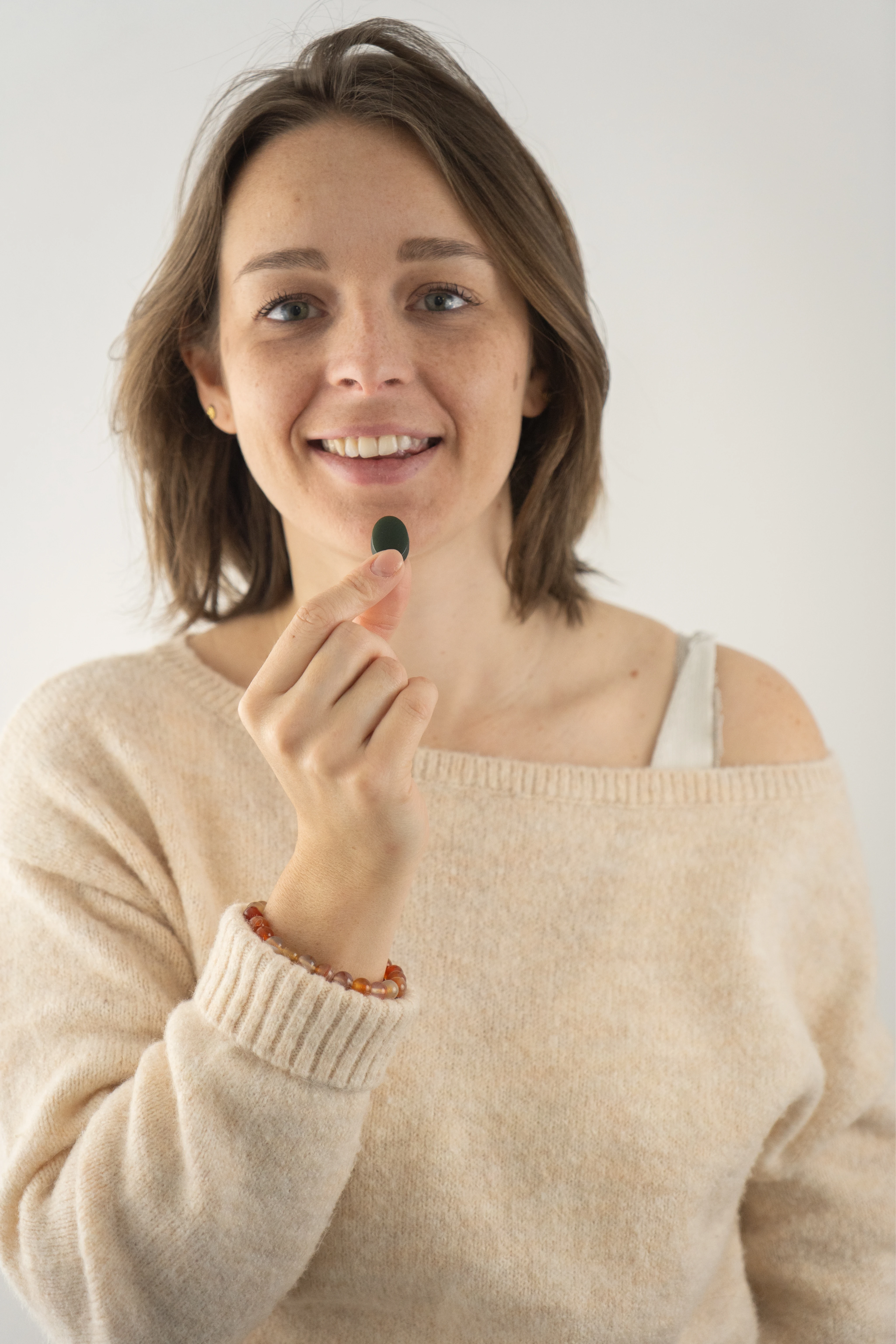 Jeune femme souriante tenant une capsule noire entre le pouce et l'index devant un fond clair.