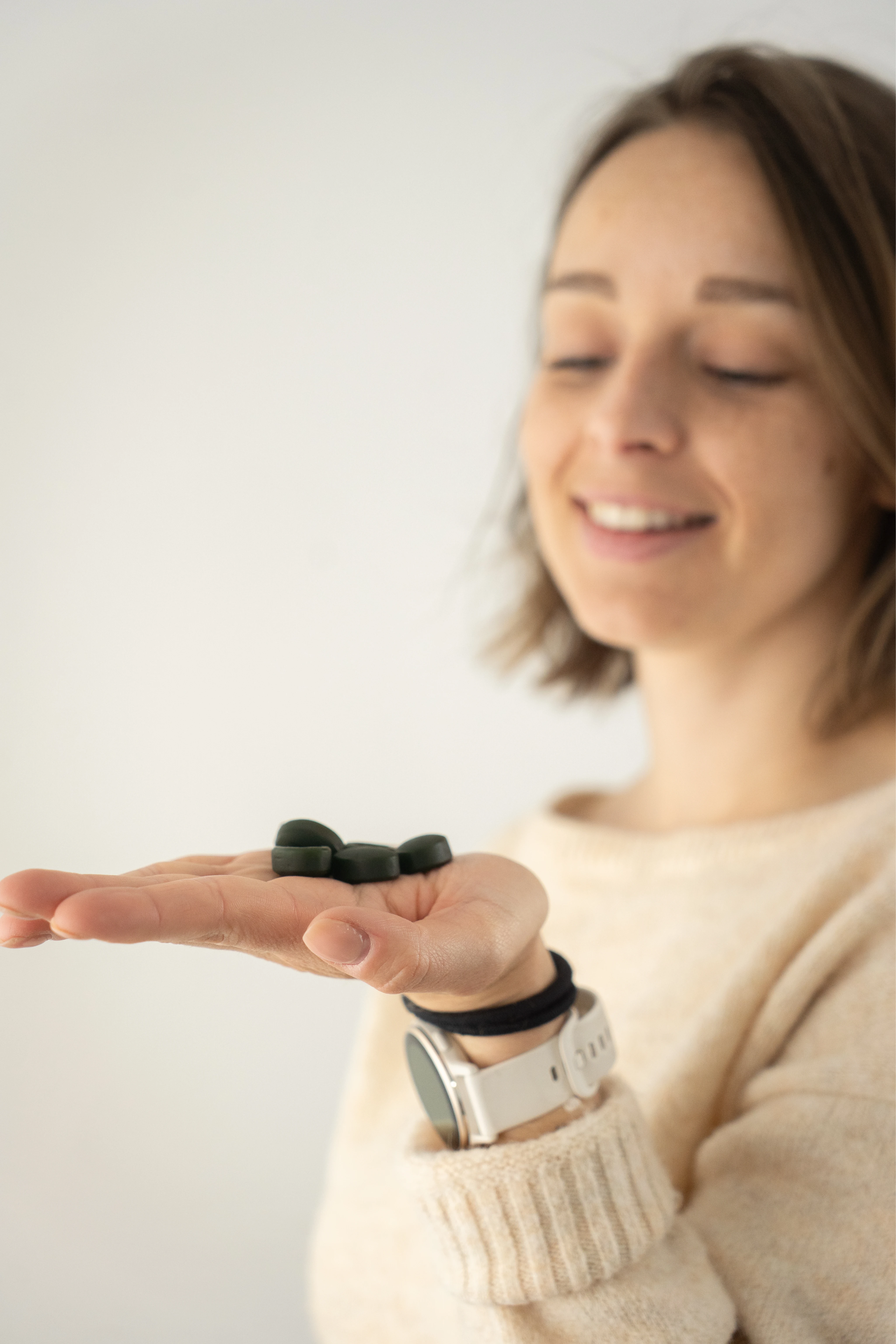 Femme souriante tenant des comprimés noirs dans la paume de sa main ouverte.