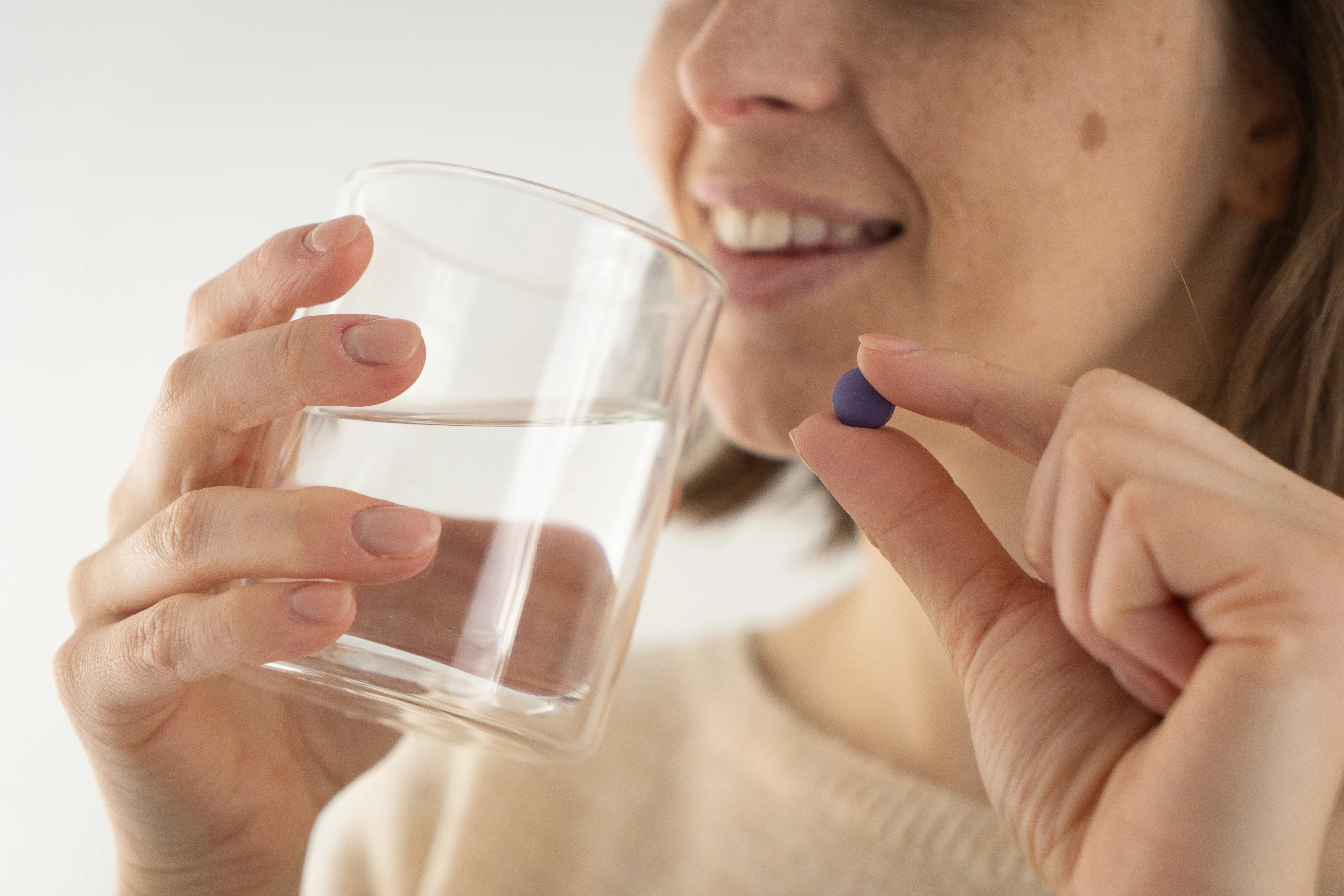 Femme tenant une petite pilule bleue entre le pouce et l'index avec un verre d'eau dans l'autre main, prête à la prendre.