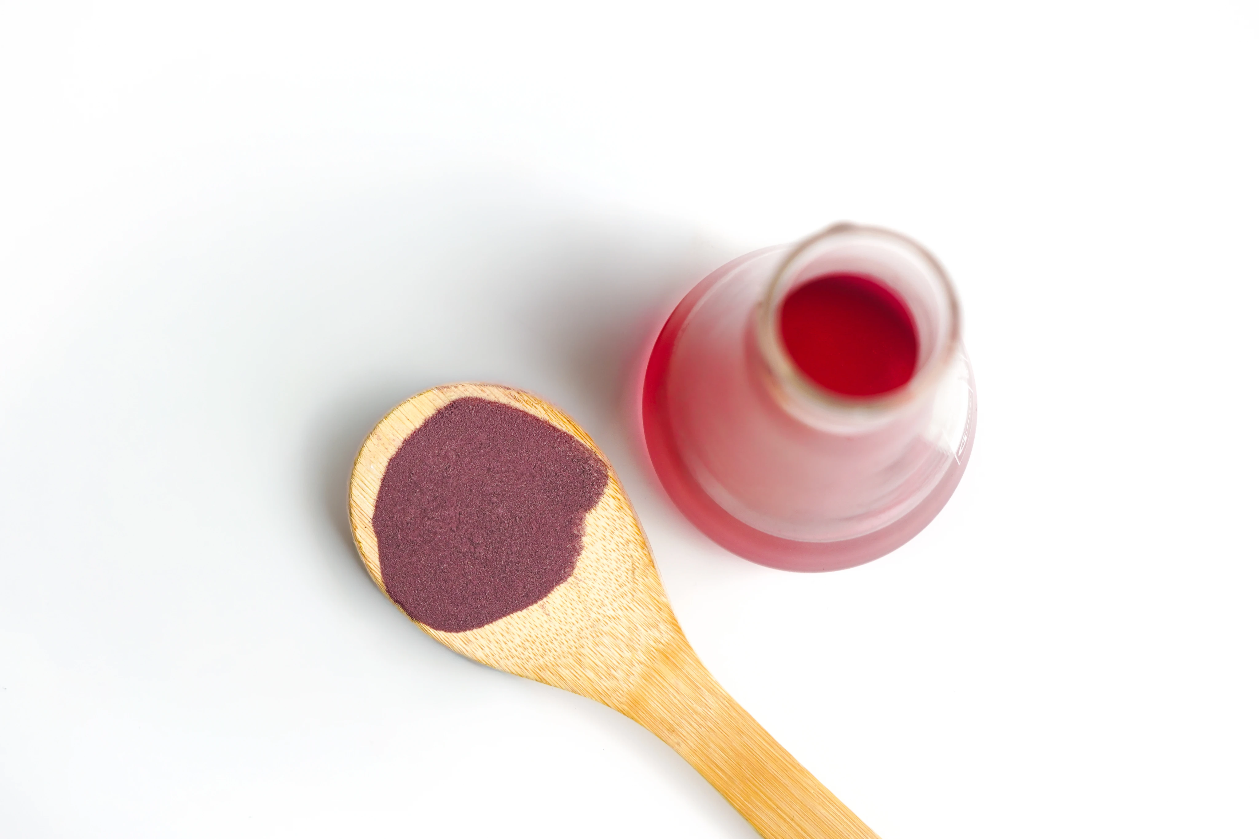 Cuillère en bois avec poudre violette et flacon en verre partiellement rempli de liquide rouge.