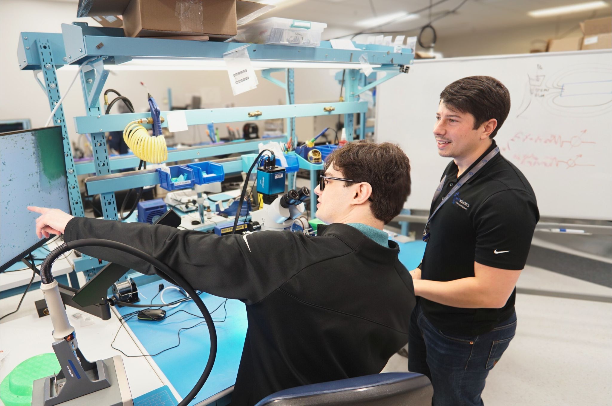 Two men collaborating in a lab while one points at a computer screen and the other watches.