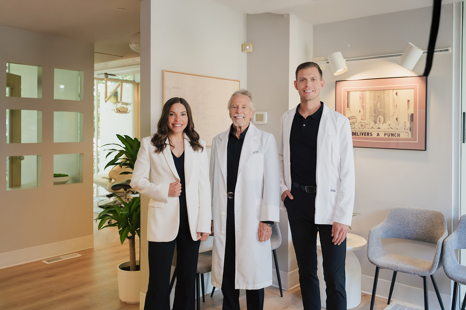 Three medical professionals wearing white coats standing and smiling in a bright, modern office.