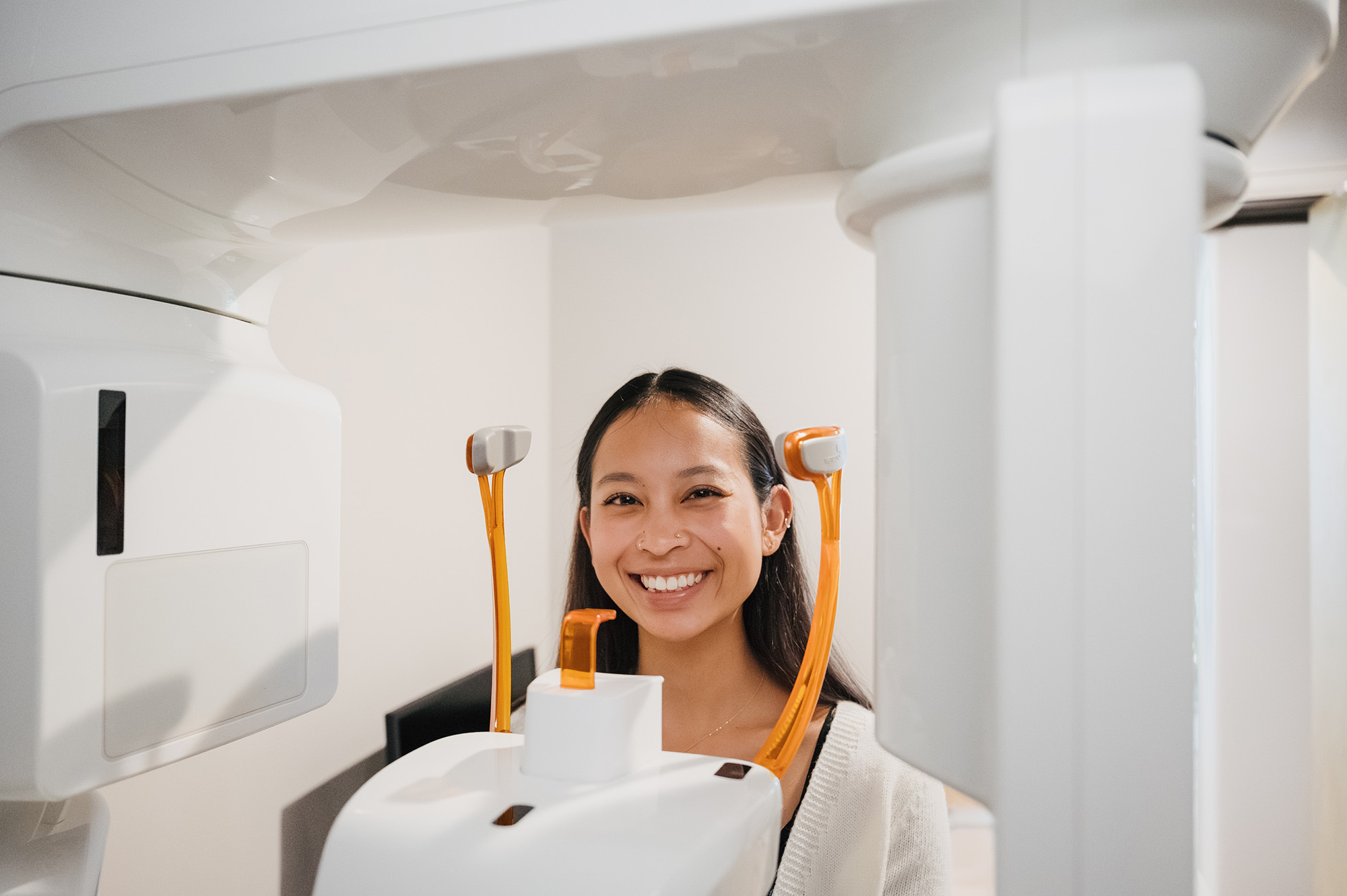Smiling woman undergoing a dental or medical scan with white and orange scanning equipment.