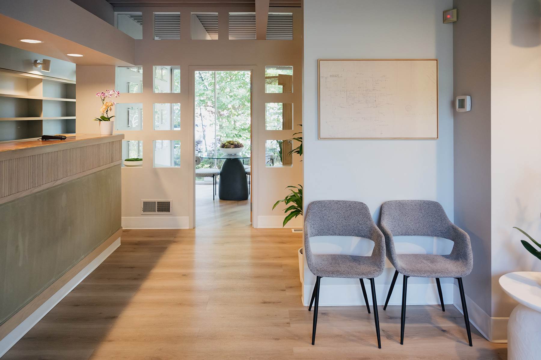 Modern reception area with two gray chairs, wooden floor, and a decorative orchid on the counter.