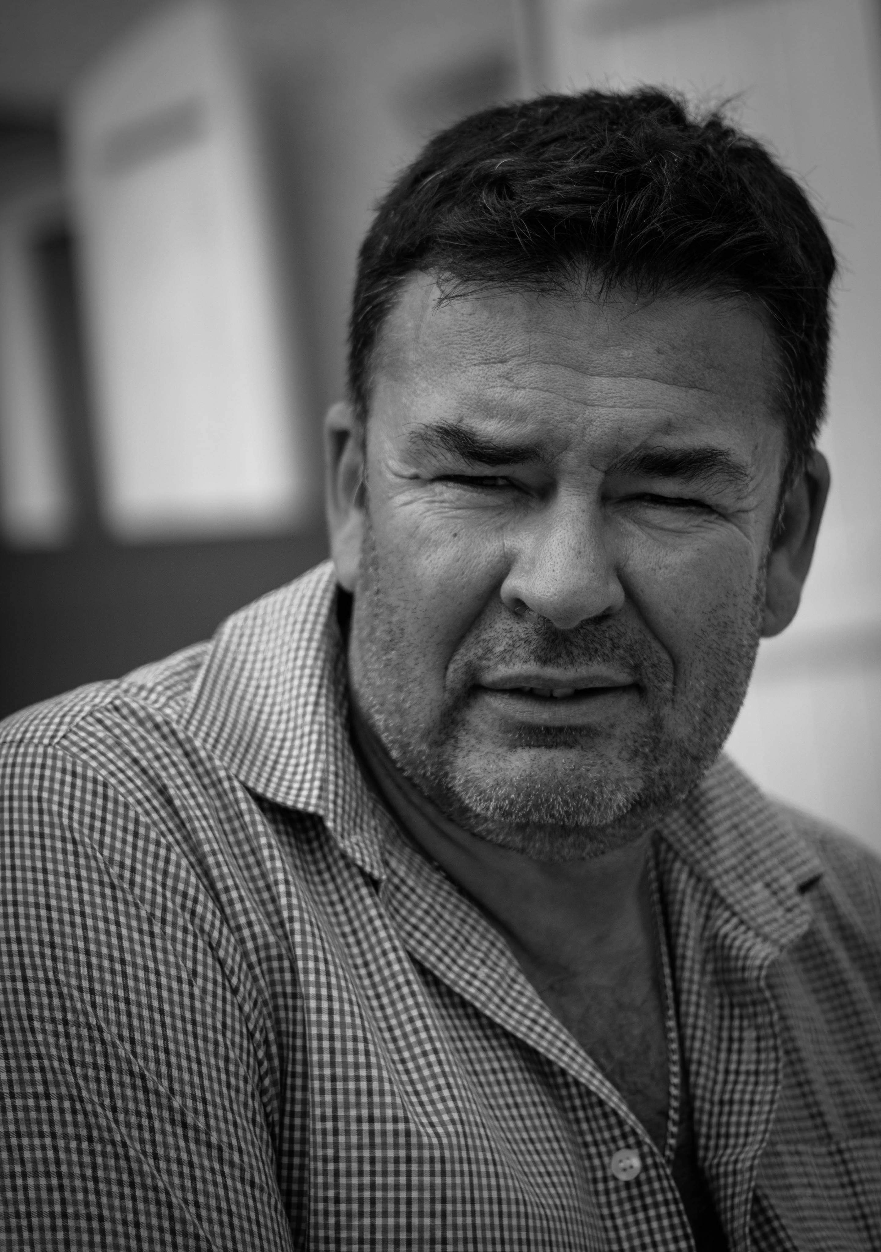 Portrait en noir et blanc d'un homme d'âge moyen avec une chemise à carreaux regardant vers l'avant.