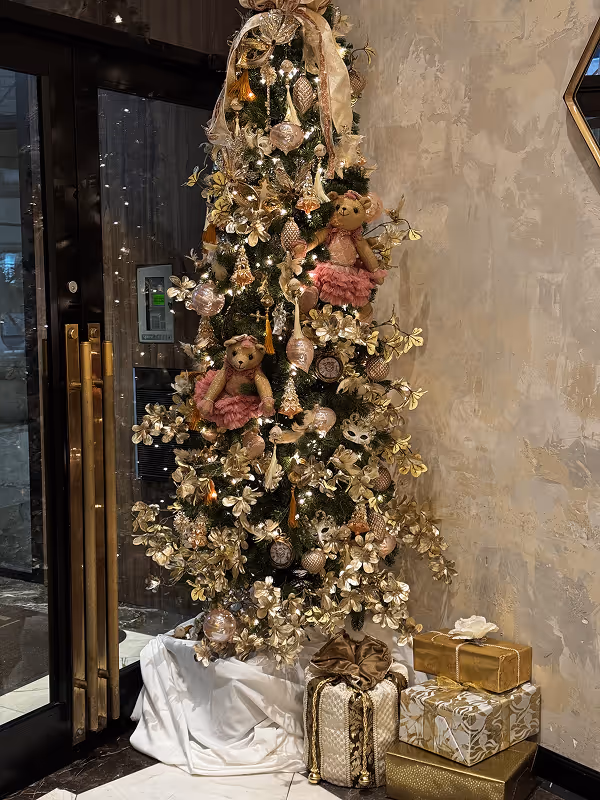 Decorated Christmas tree with gold flowers, ornaments, two teddy bears in pink skirts, and wrapped gifts underneath.