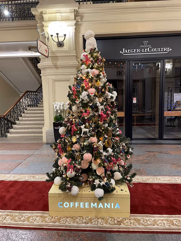 Decorated Christmas tree with pink, white, and brown ornaments and a white knit hat on top, placed on a box indoor shopping area.