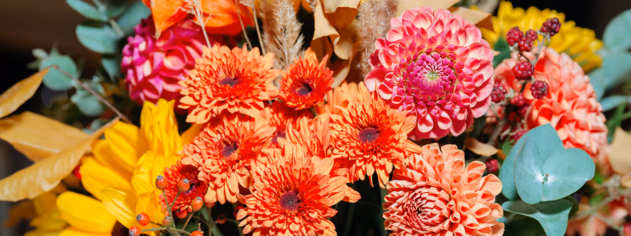 Bright bouquet featuring orange and pink dahlias, yellow sunflowers, red berries, green eucalyptus leaves, and dried grasses.
