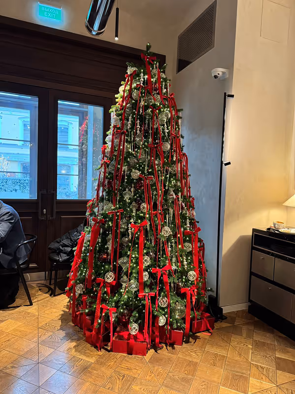 Tall Christmas tree decorated with white lights, red ribbons, silver ornaments, and red gift boxes.