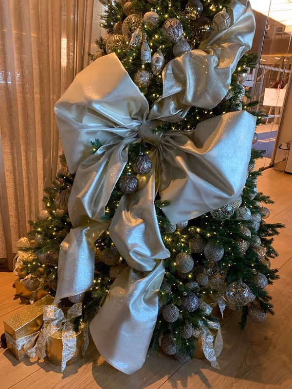 Decorated Christmas tree with large silver bows, silver ornaments, and wrapped gifts underneath.
