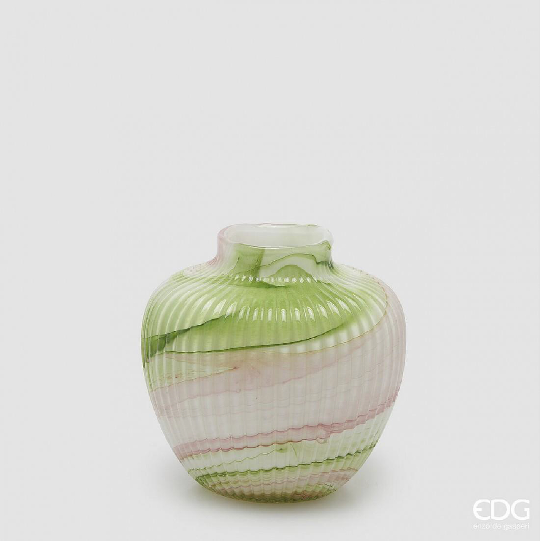 A compact glass vase with a rounded form and soft green mix tones layered through a ribbed texture. The gentle color transitions, combined with subtle pink accents, create a calm and balanced look. Its sculptural shape makes it suitable for small floral arrangements or as a decorative piece that adds texture and warmth to shelves, tables, or consoles. 