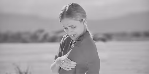 Woman outdoors clutching her upper arm with a pained expression.