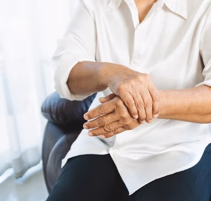 Person in a white shirt sitting and holding their wrist, suggesting wrist pain or discomfort.