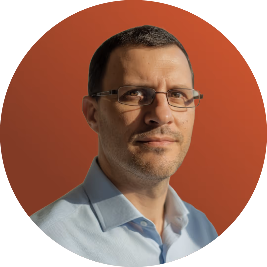 Un homme portant des lunettes et une chemise bleu clair se détache sur un fond circulaire orange, regardant l'objectif avec assurance et une expression neutre.