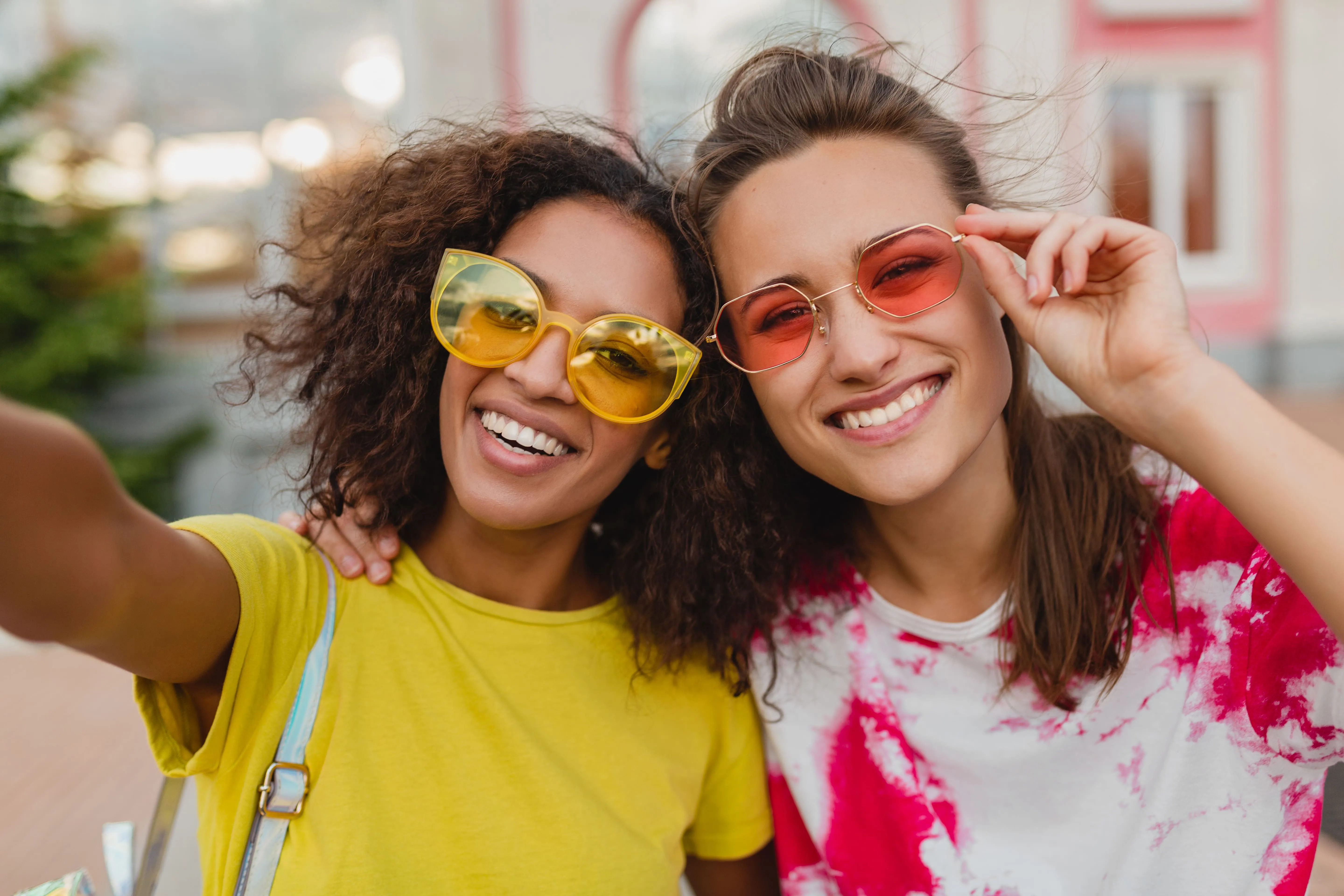 Two smiling women wearing colorful sunglasses taking a selfie outdoors