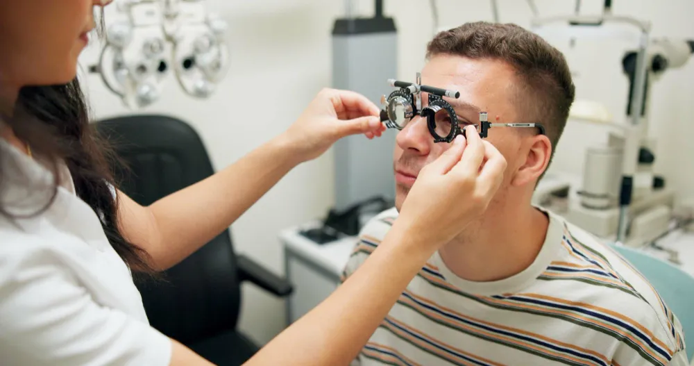 Optometrist fitting trial frame eyeglasses on male patient in exam room