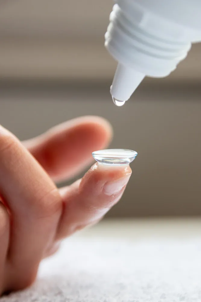 Hand holding contact lens with dropper dispensing solution above
