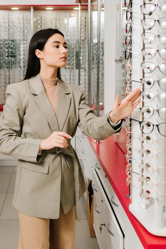Woman browsing eyeglasses display in optical store wearing beige blazer