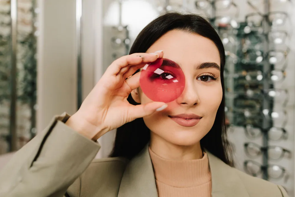 Woman holding red glass sphere in front of eye at eyeglasses shop